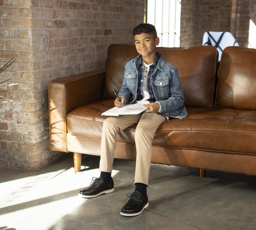 Shop Florsheim Kids featuring a child sitting on a leather sofa.