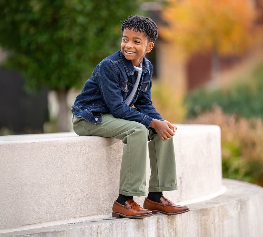 Shop Florsheim kids featuring a kid sitting on a step wearing cognac loafers.