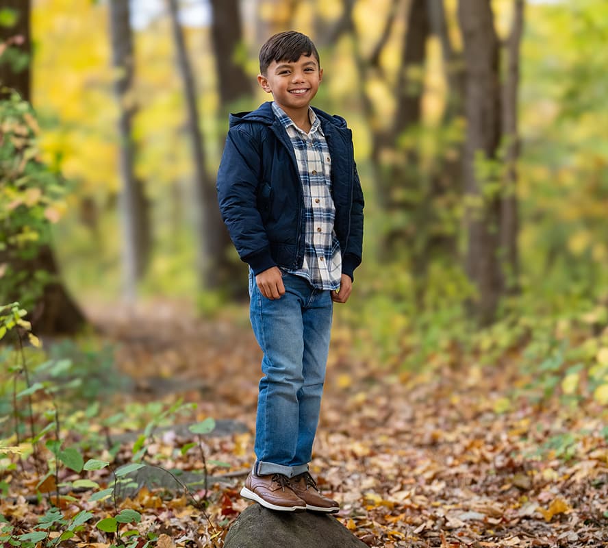 Shop the Florsheim Kids Category featuring a kid standing in the forest on a log wearing the Great Lakes in cognac.