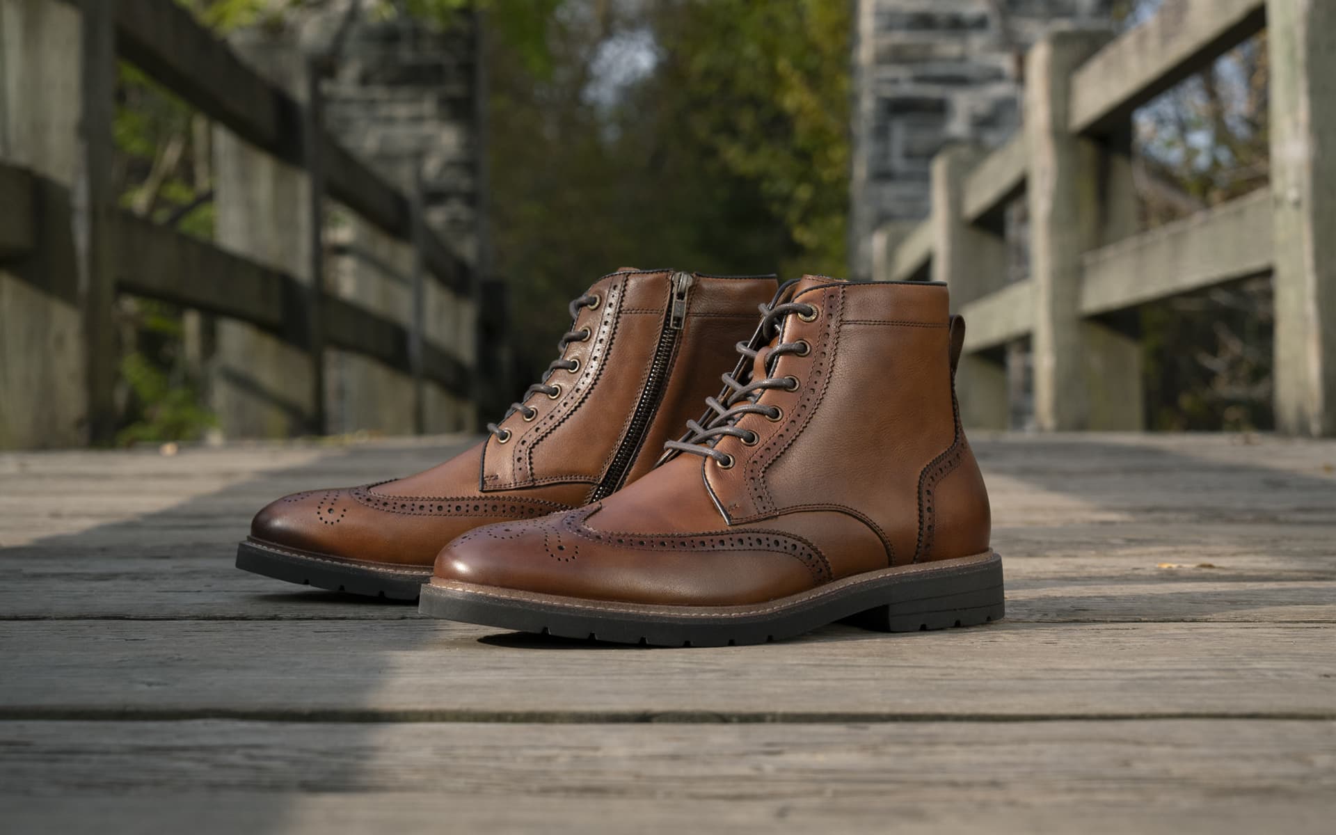 Shop Florsheim's Boot category featuring the Redford Wingtip Lace Up Boot in Cognac on a wooden bridge.
