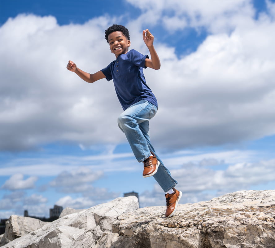 Shop Florsheim kids featuring the Fleet perf slip on sneaker on a kid jumping off a rock.