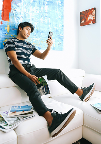 Image of social media influencer Marco Arrieta sitting on a couch wearing the Crossover Lace To Toe Sneaker in Black.