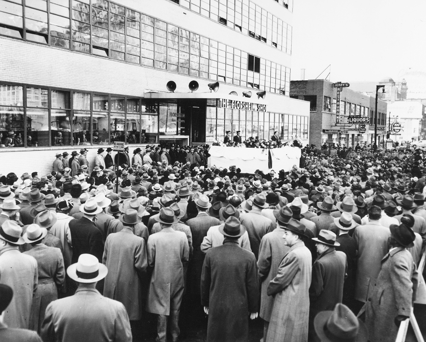 The image is of a crowd gathered in front of the new Florsheim factory in Chicago as part of the unveiling ceremony in 1949.